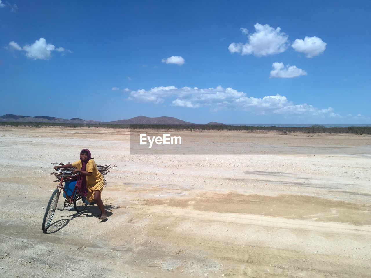 Woman carrying firewood on bicycle against blue sky at desert