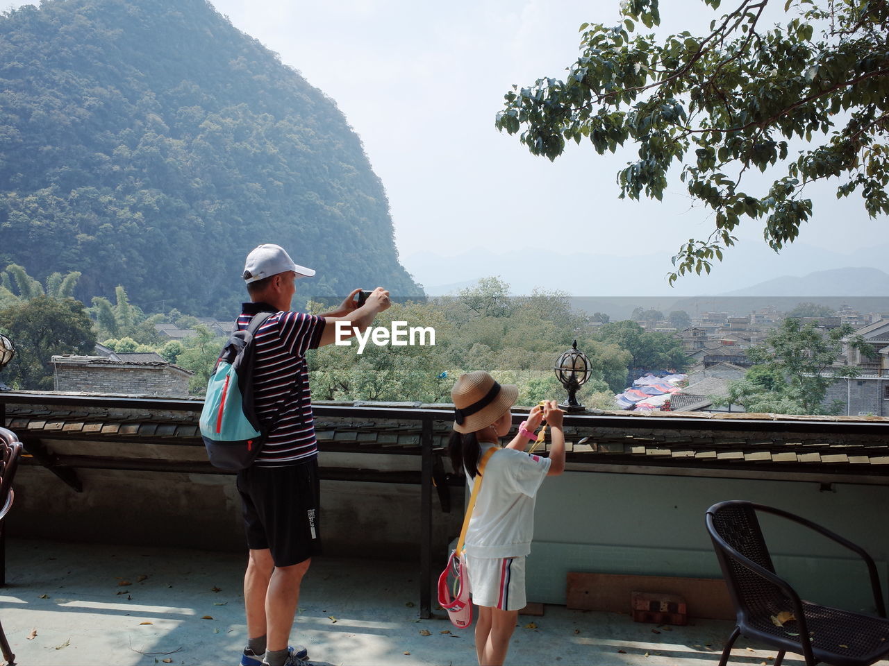 Rear view of people standing on mountain against sky,  a child and her grnadtook photos
