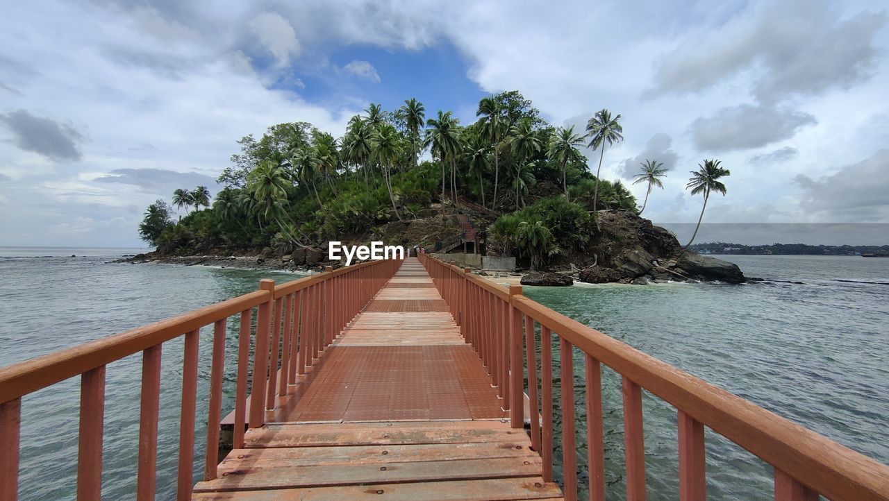 View of the mystical island at the end of the wooden boardwalk surrounded by the blue sea 