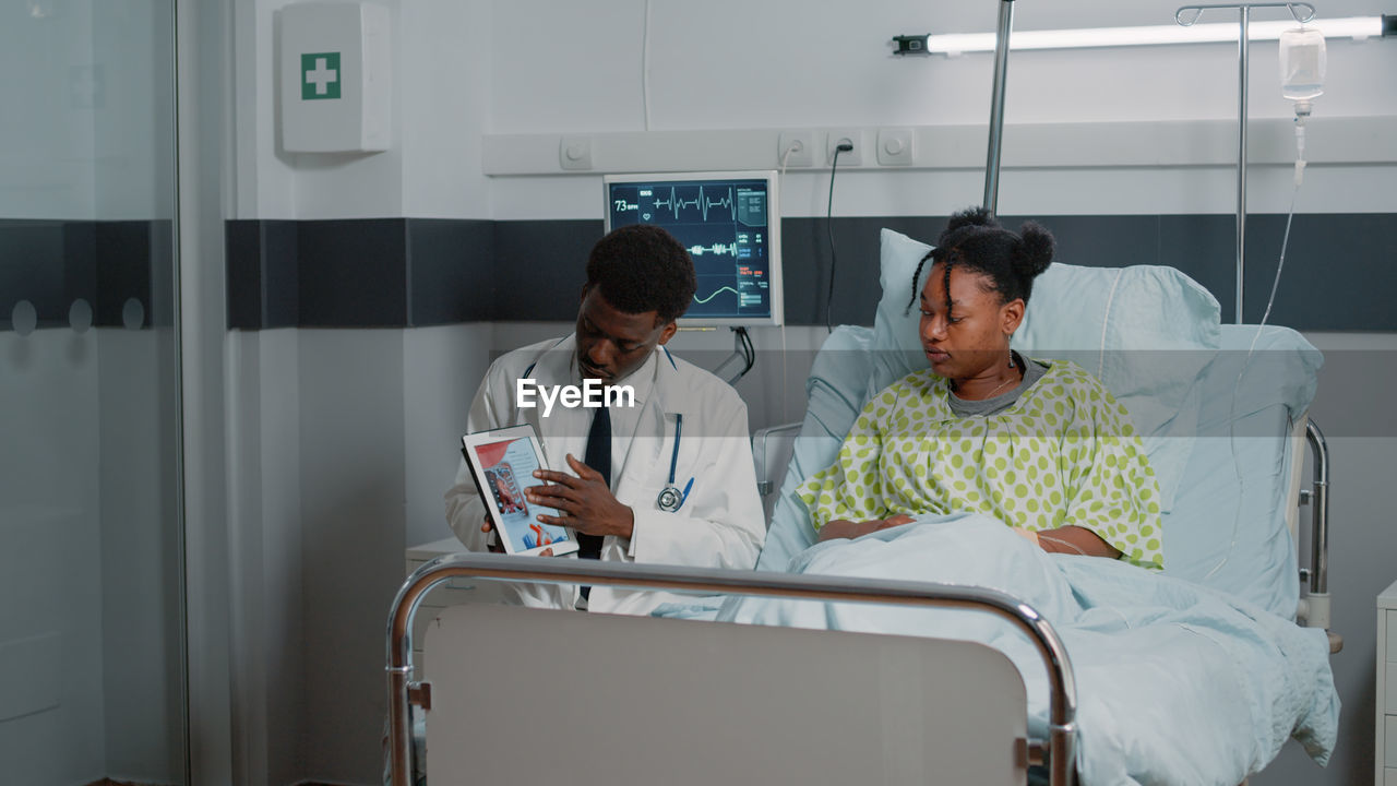 Doctor showing test result on tablet pc to patient in ward at hospital