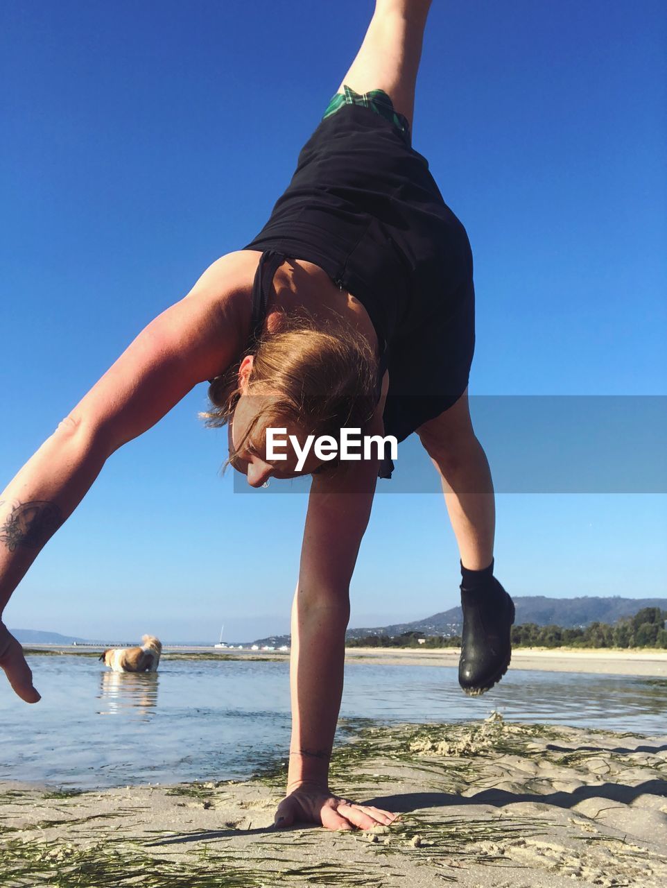 Woman practicing handstand at beach against clear sky