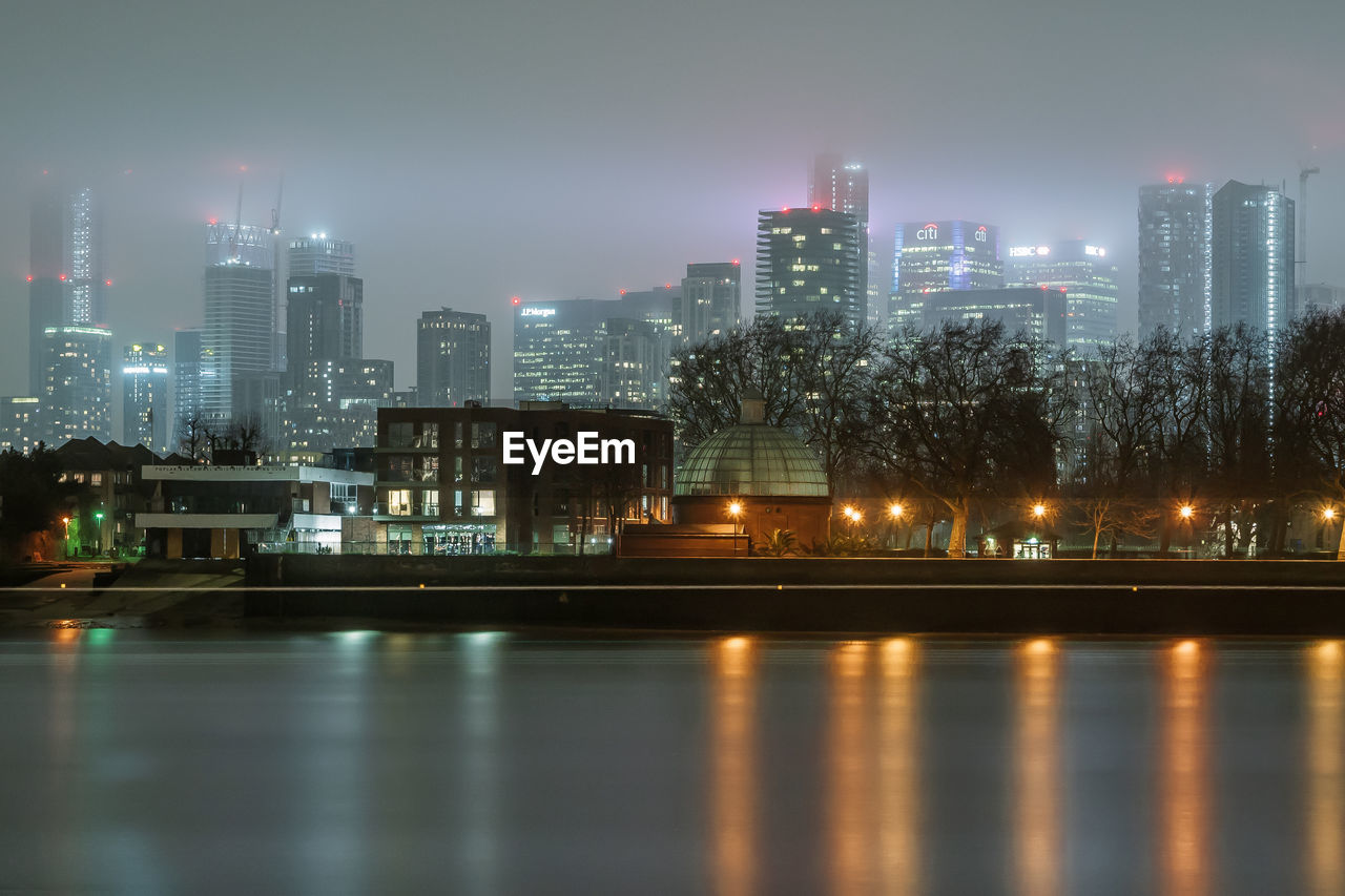 Illuminated city by river against sky at night