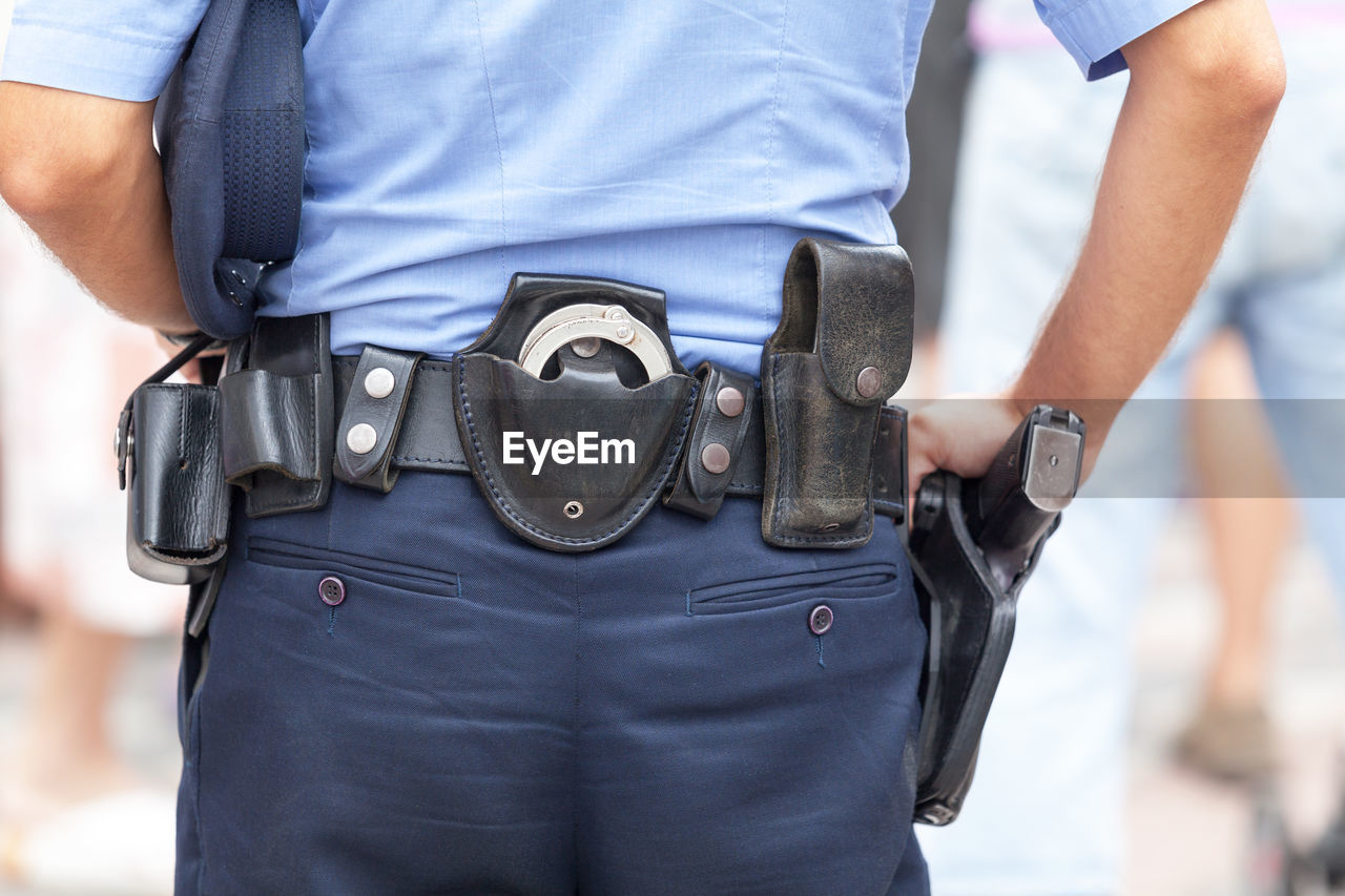Midsection rear view of police man with belt with handcuffs and gun