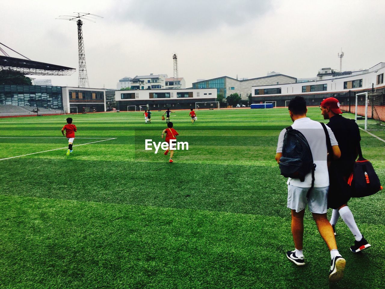 REAR VIEW OF PEOPLE ON SOCCER FIELD AGAINST SKY