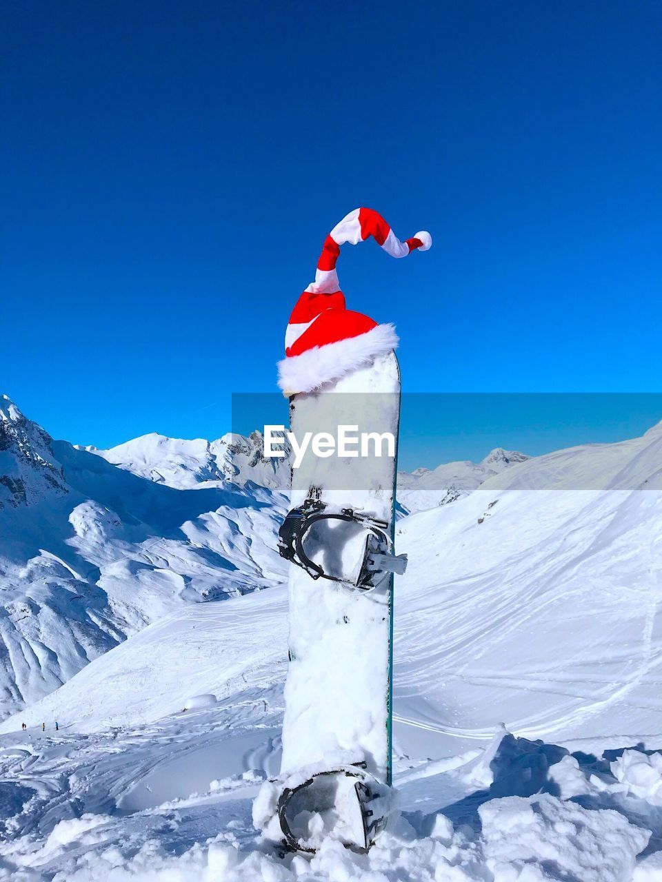 Santa hat on equipment at snowcapped mountain against clear blue sky