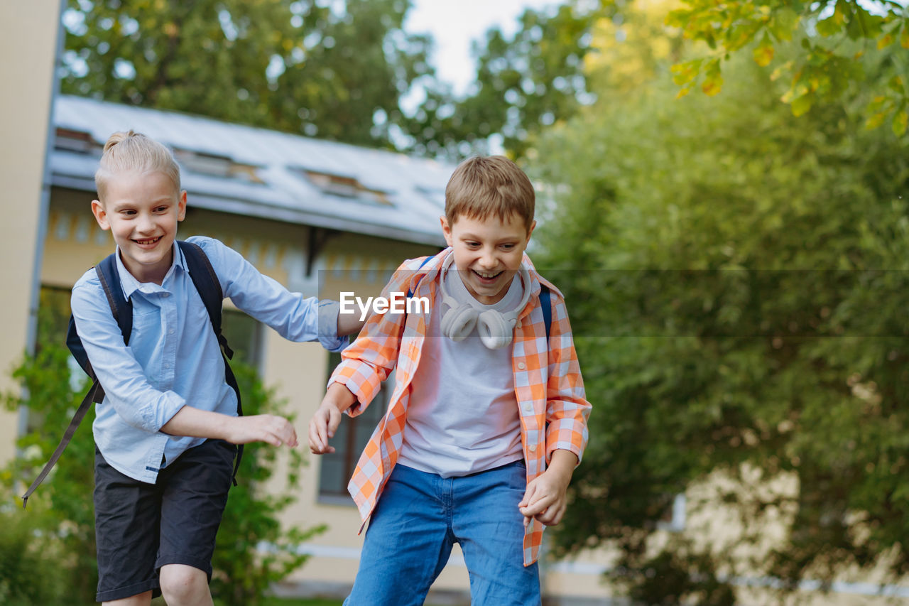 Happy caucasian children running from school with backpacks on sunny day. begining of academic year.