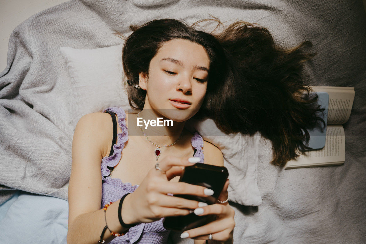 Directly above shot of woman using smart phone while lying on bed at home