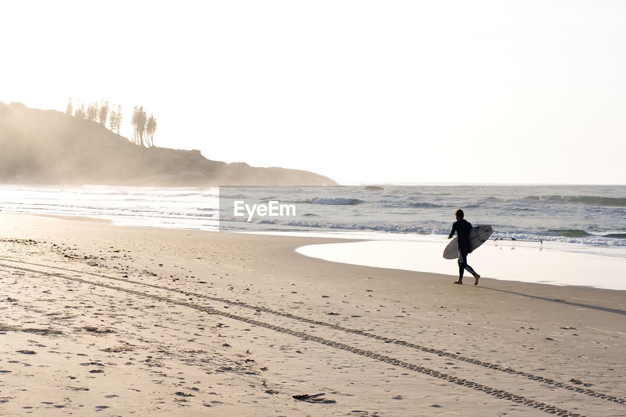 Unrecognizable man running with surf board at the beach