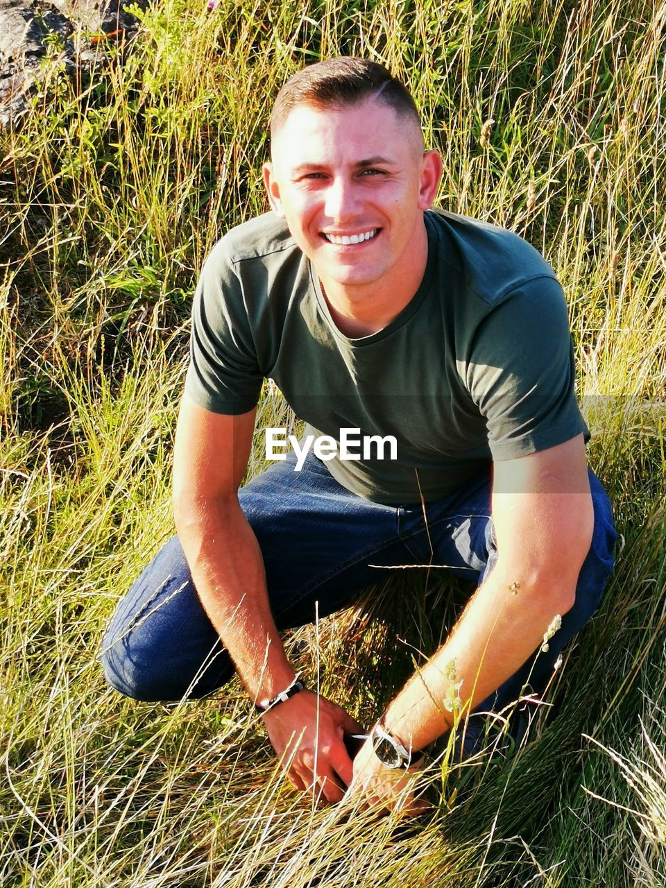 PORTRAIT OF SMILING MAN SITTING ON FIELD