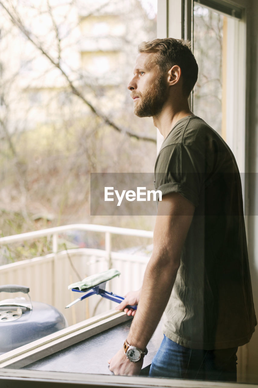Side view of thoughtful man looking through window