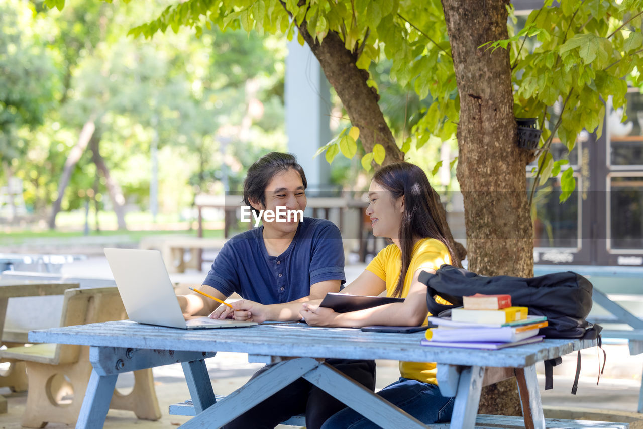 Couple of students sitting and using laptop in outdoor university doing some online research