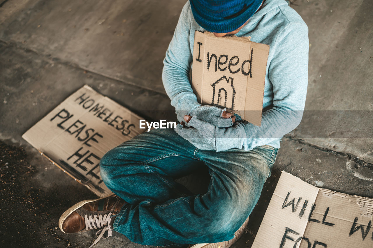 HIGH ANGLE VIEW OF MAN SITTING ON STREET WITH TEXT