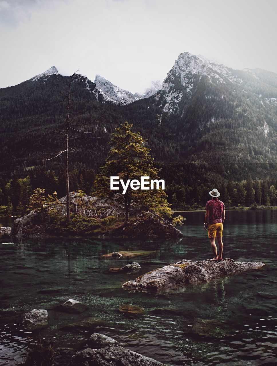 Rear view of man standing amidst lake on rock