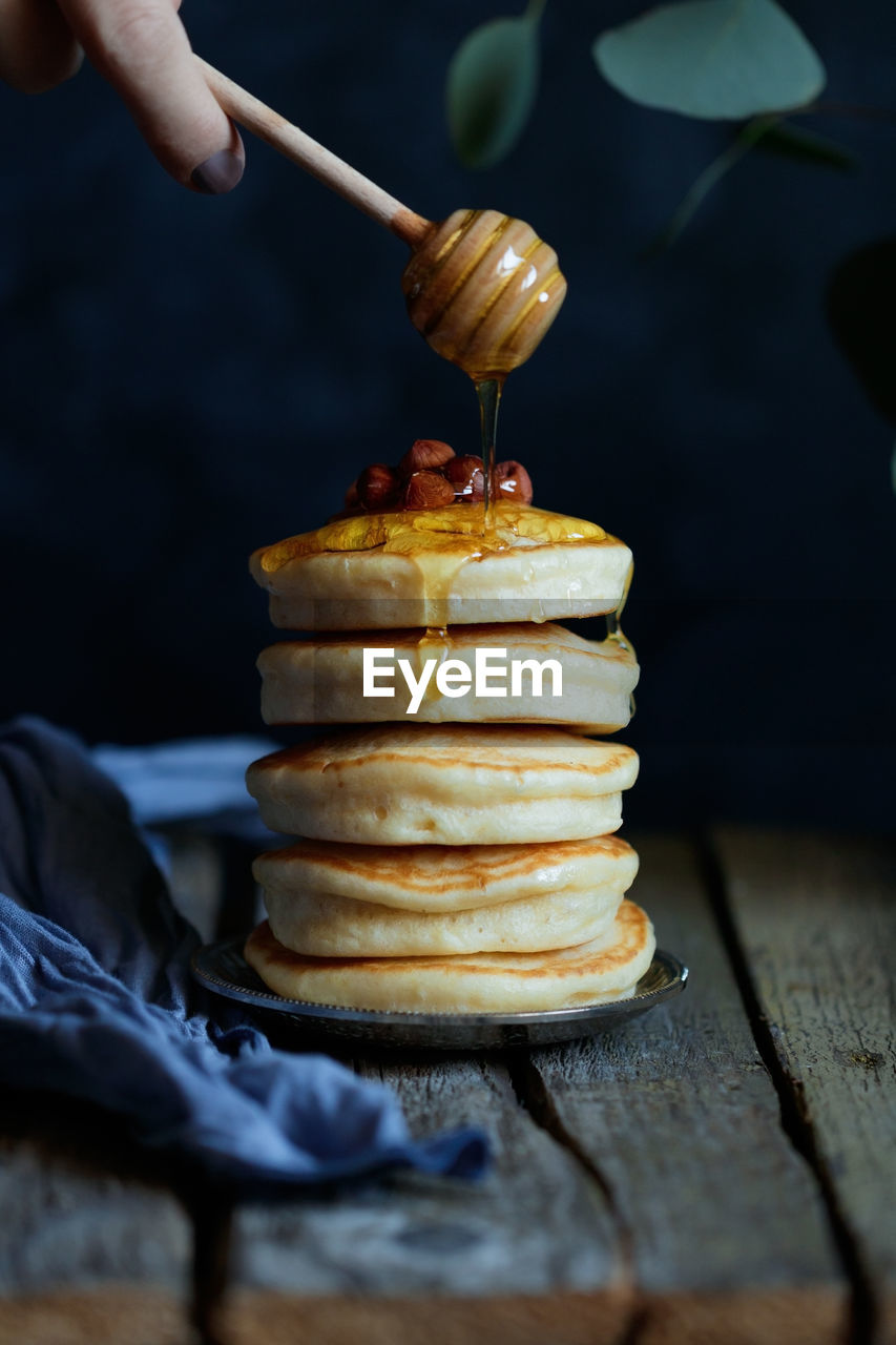 Cropped hand pouring honey on pancakes stacked on table