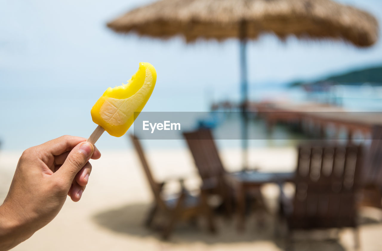 Cropped hand holding ice pop at beach