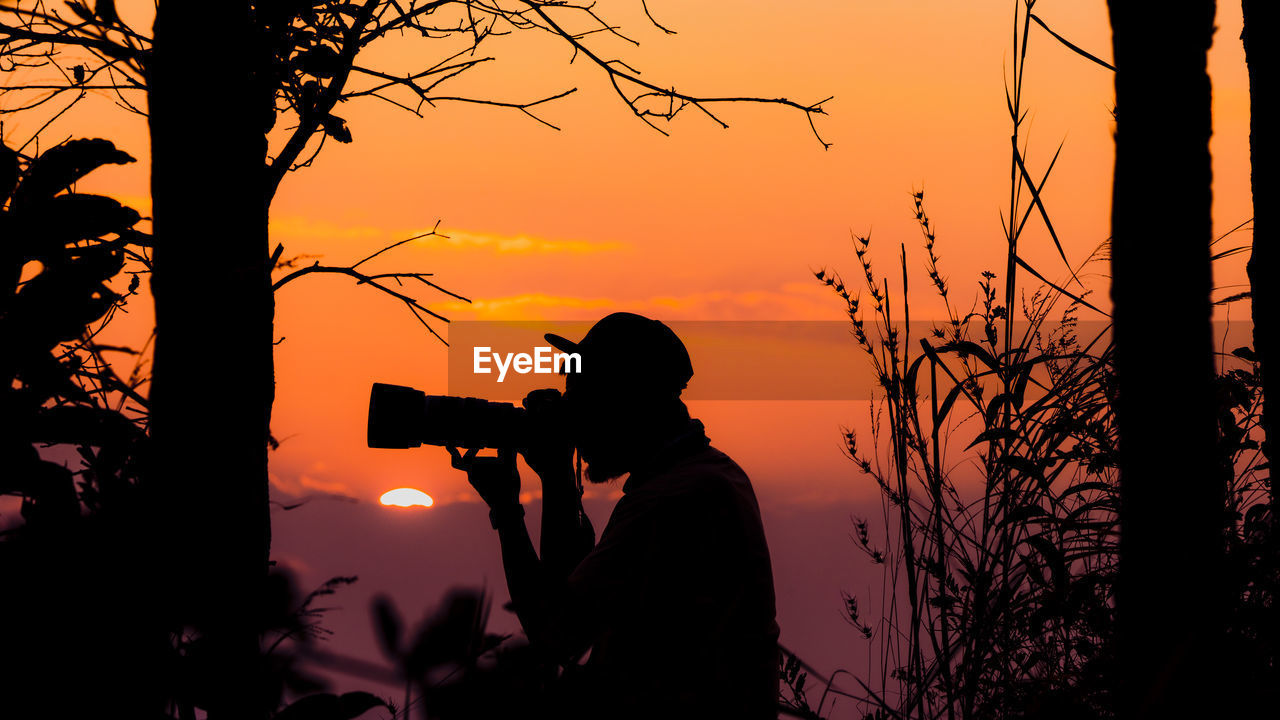 Silhouette man photographing against sky during sunset