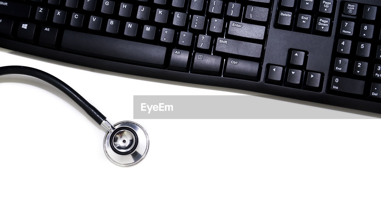 Close-up of computer keyboard and stethoscope over white background