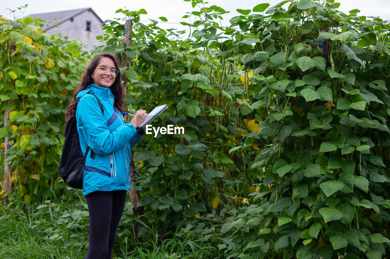 portrait of smiling young woman standing against plants