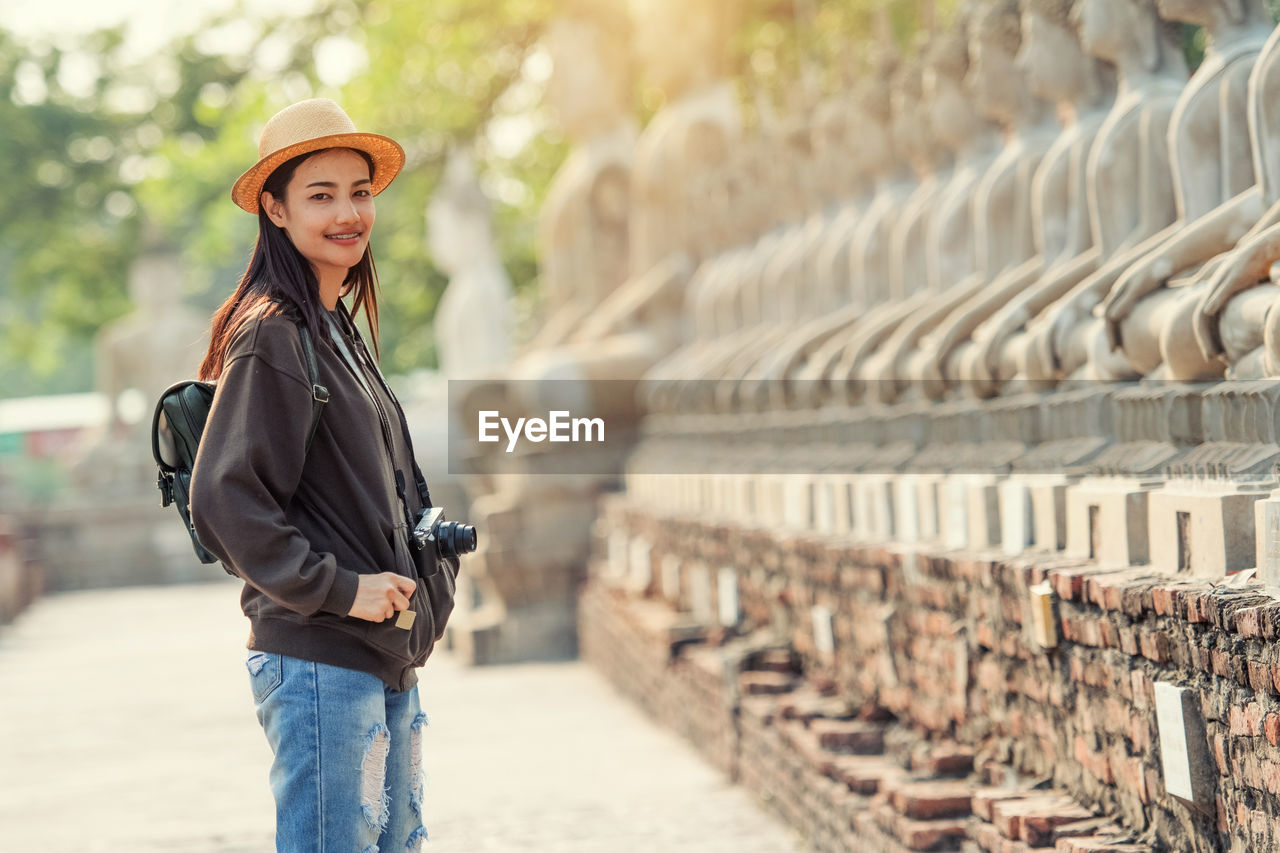 Portrait of young woman with camera standing outdoors