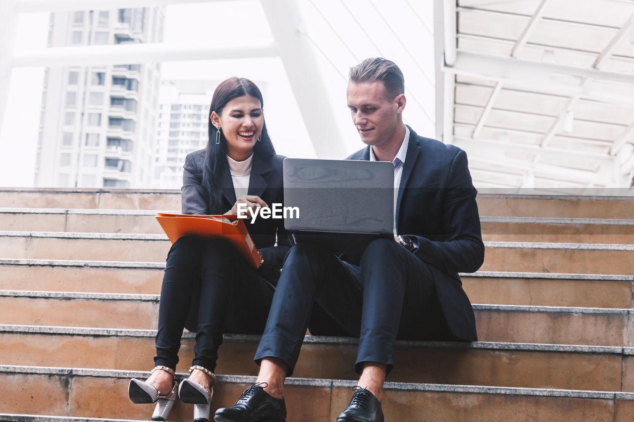 Low angle view of colleagues discussing while sitting on steps in city