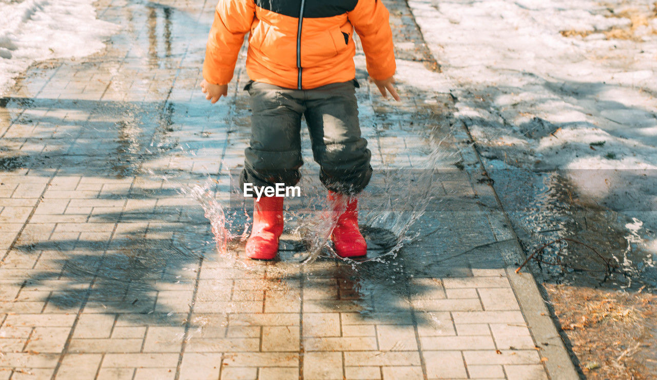 Gleeful puddles, red boots send cascade of droplets, celebration of melting snow on sunny day