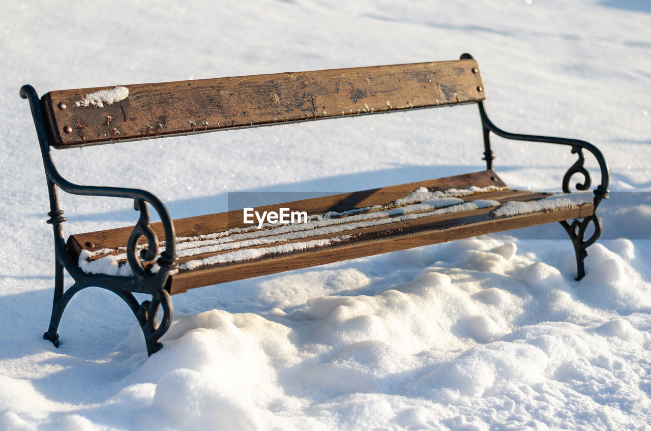 EMPTY BENCH IN SNOW COVERED FIELD