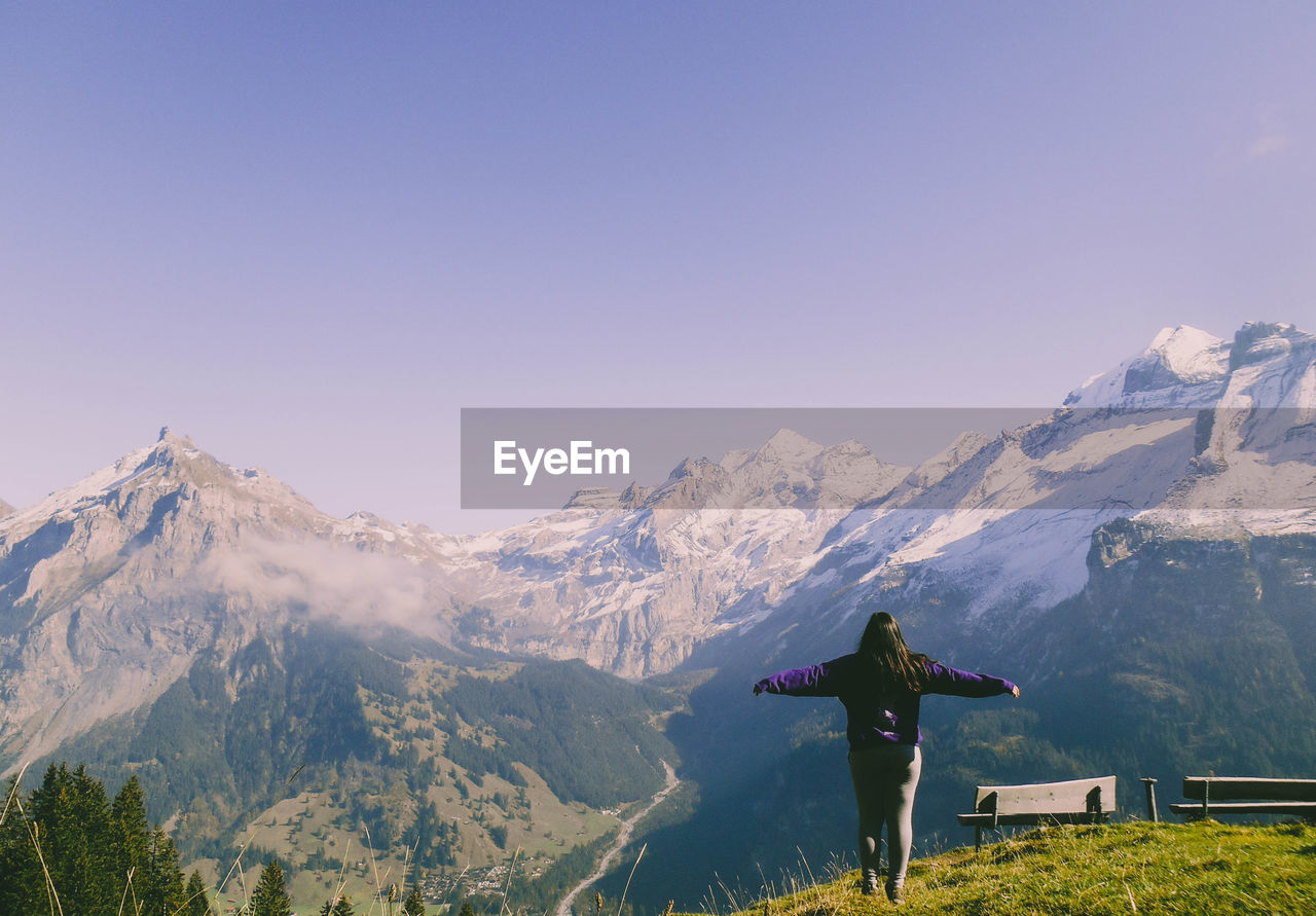 Rear view of woman with arms outstretched standing against snowcapped mountains