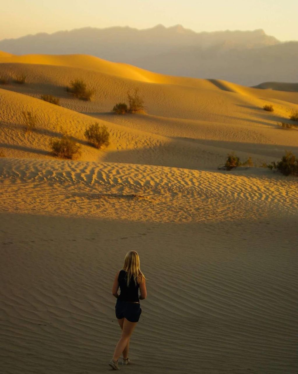 REAR VIEW OF YOUNG WOMAN STANDING IN DESERT