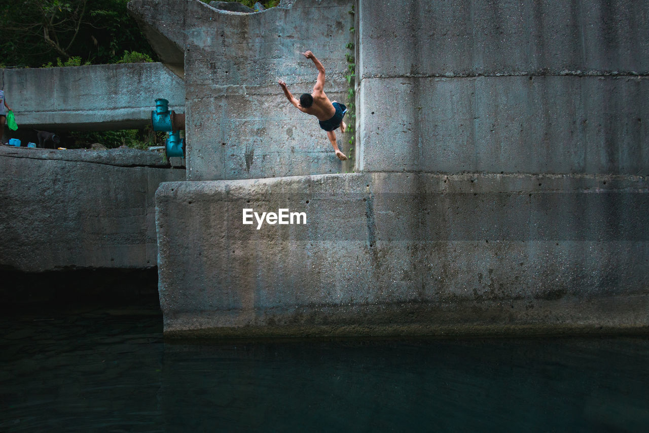 FULL LENGTH OF SHIRTLESS MAN JUMPING IN WATER