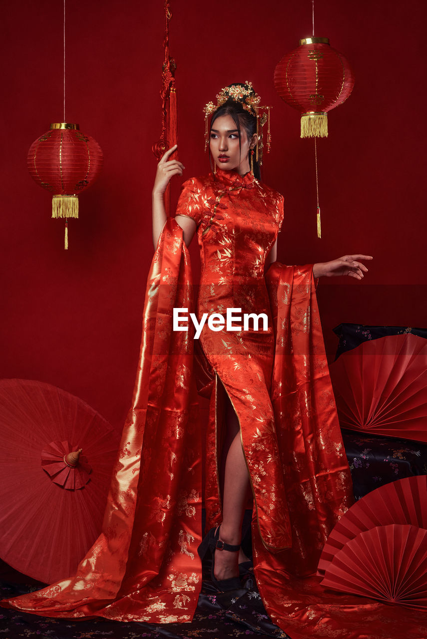 Full length portrait of woman standing against illuminated red background