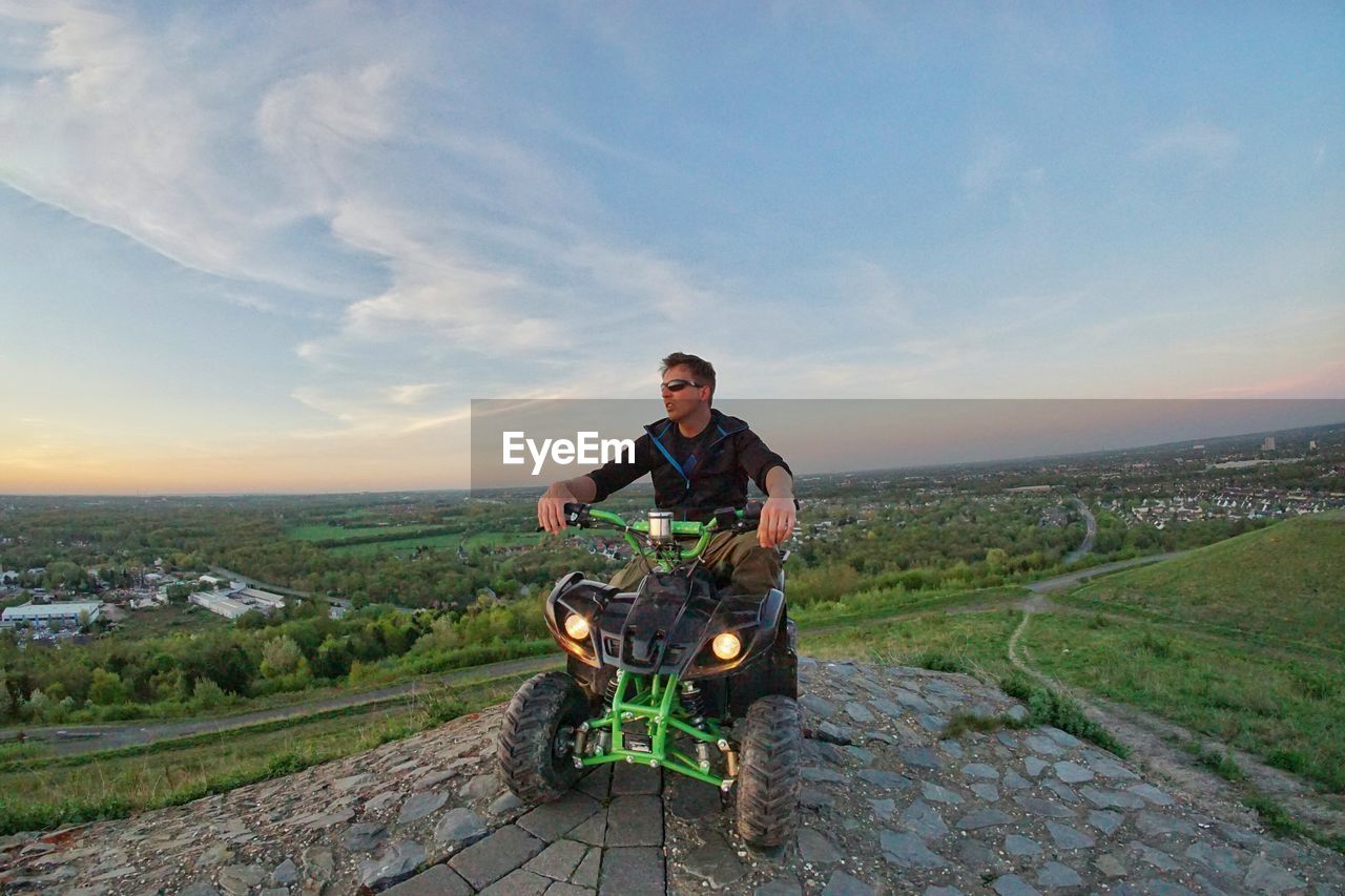 Man looking at view while riding quadbike on landscape against sky during sunset