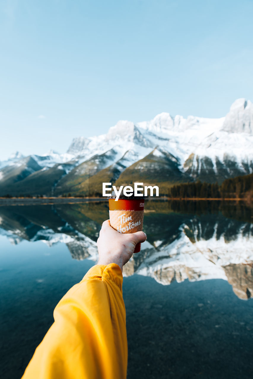 MIDSECTION OF PERSON ON SNOWCAPPED MOUNTAINS AGAINST LAKE