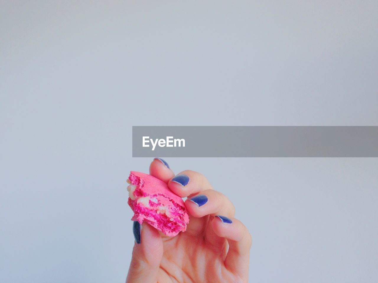 Cropped image of hand holding macaroon against gray background