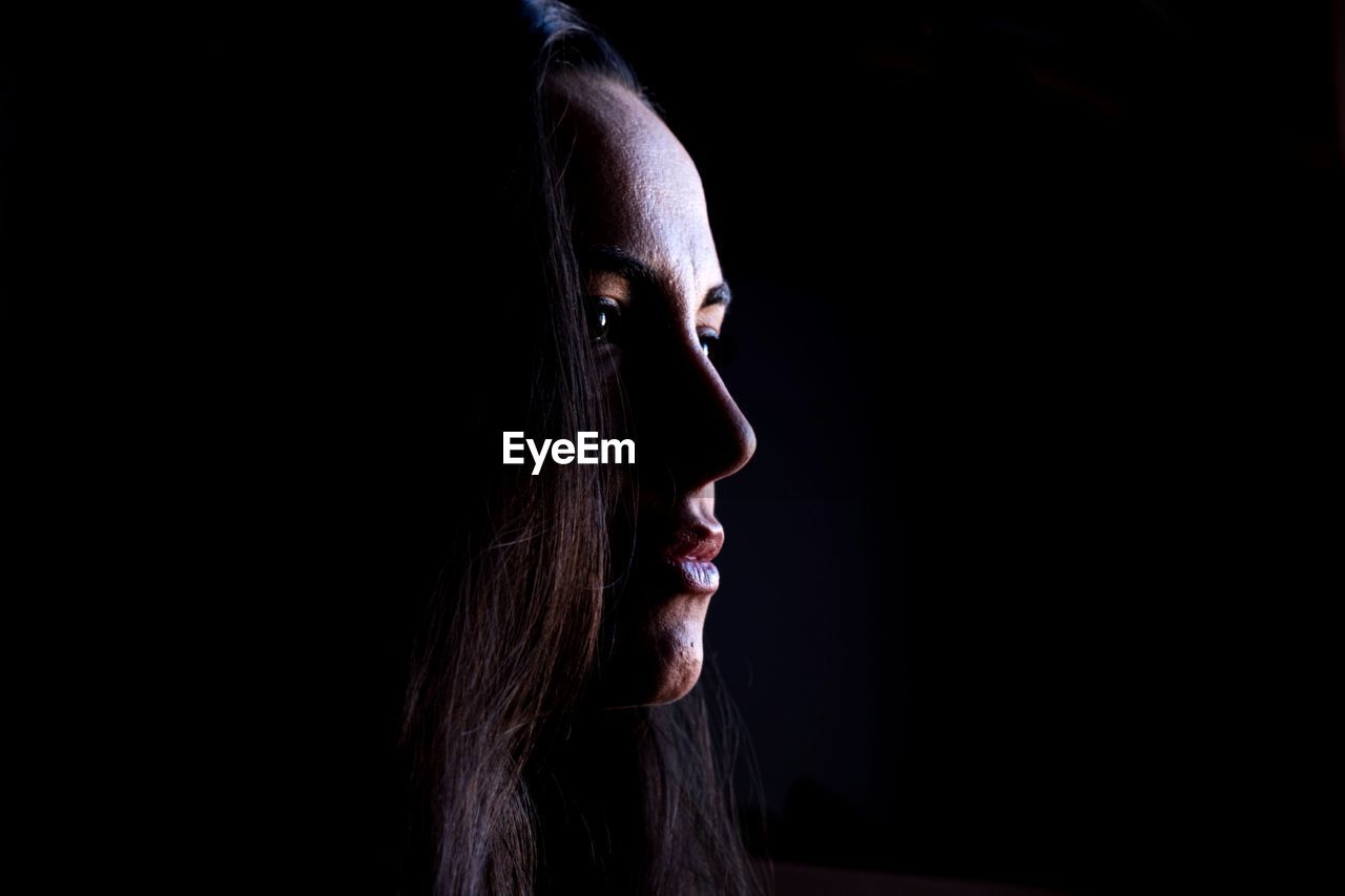 Close-up of thoughtful woman against black background