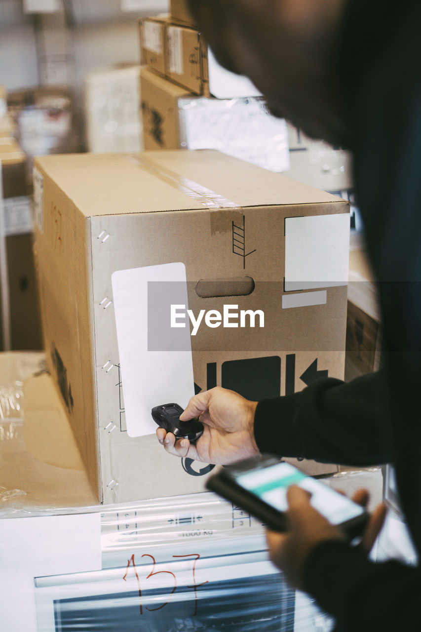 Cropped image of male worker scanning cardboard box with bar code reader at distribution warehouse