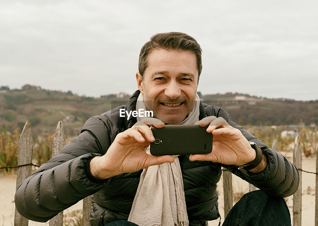 PORTRAIT OF SMILING YOUNG MAN PHOTOGRAPHING