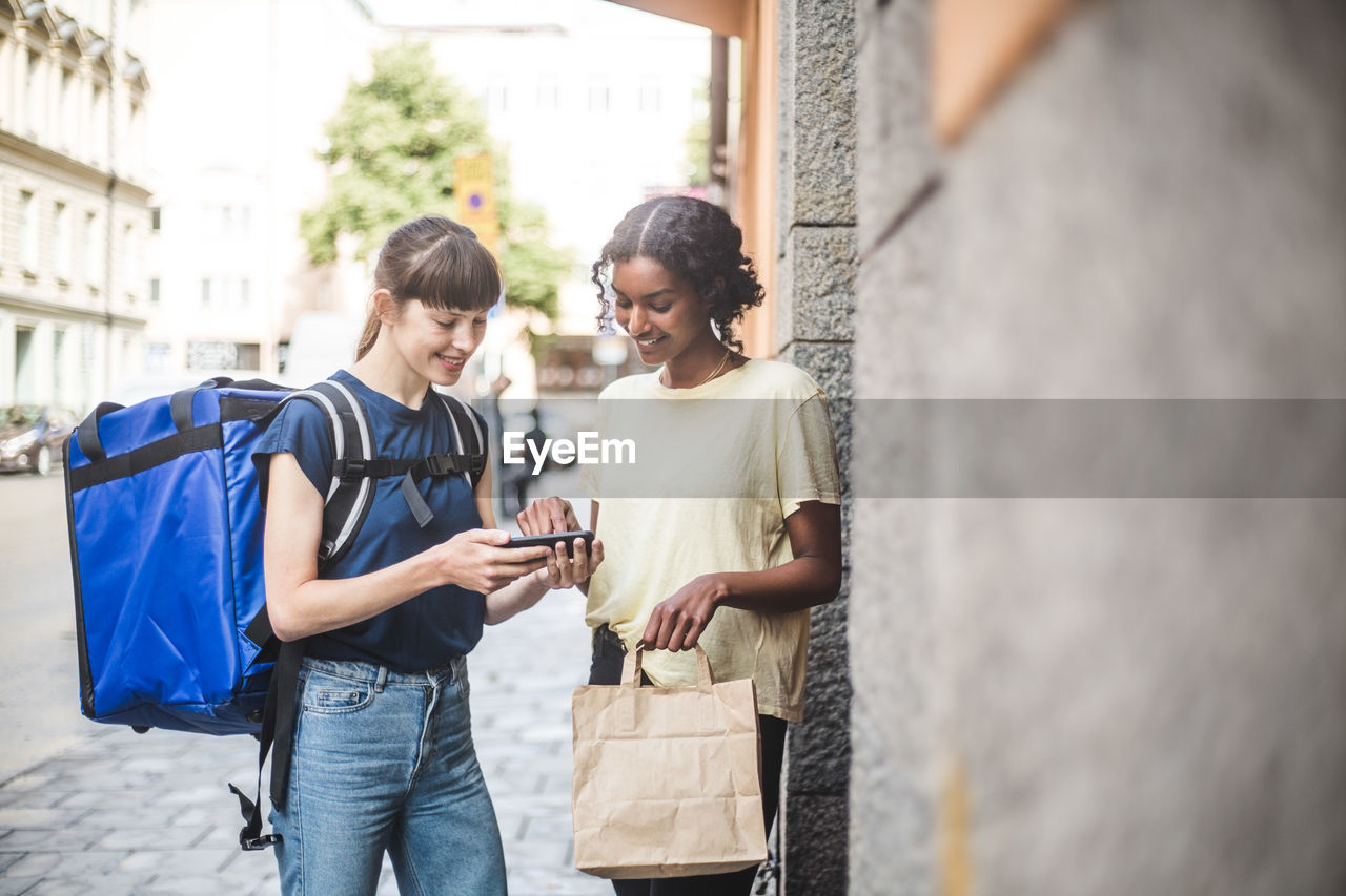 Delivery woman taking sign from female customer while delivering package