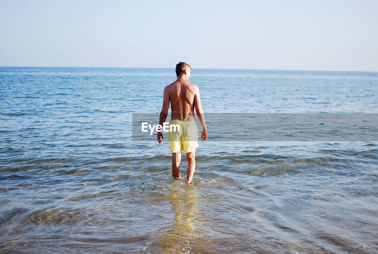 Rear view of man in yellow swim suit standing in sea against sky