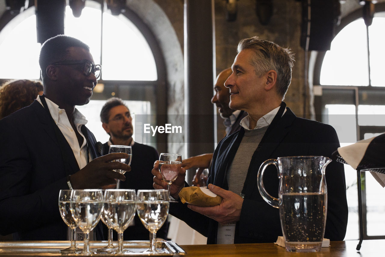 Businessmen holding glasses while discussing with each other during seminar