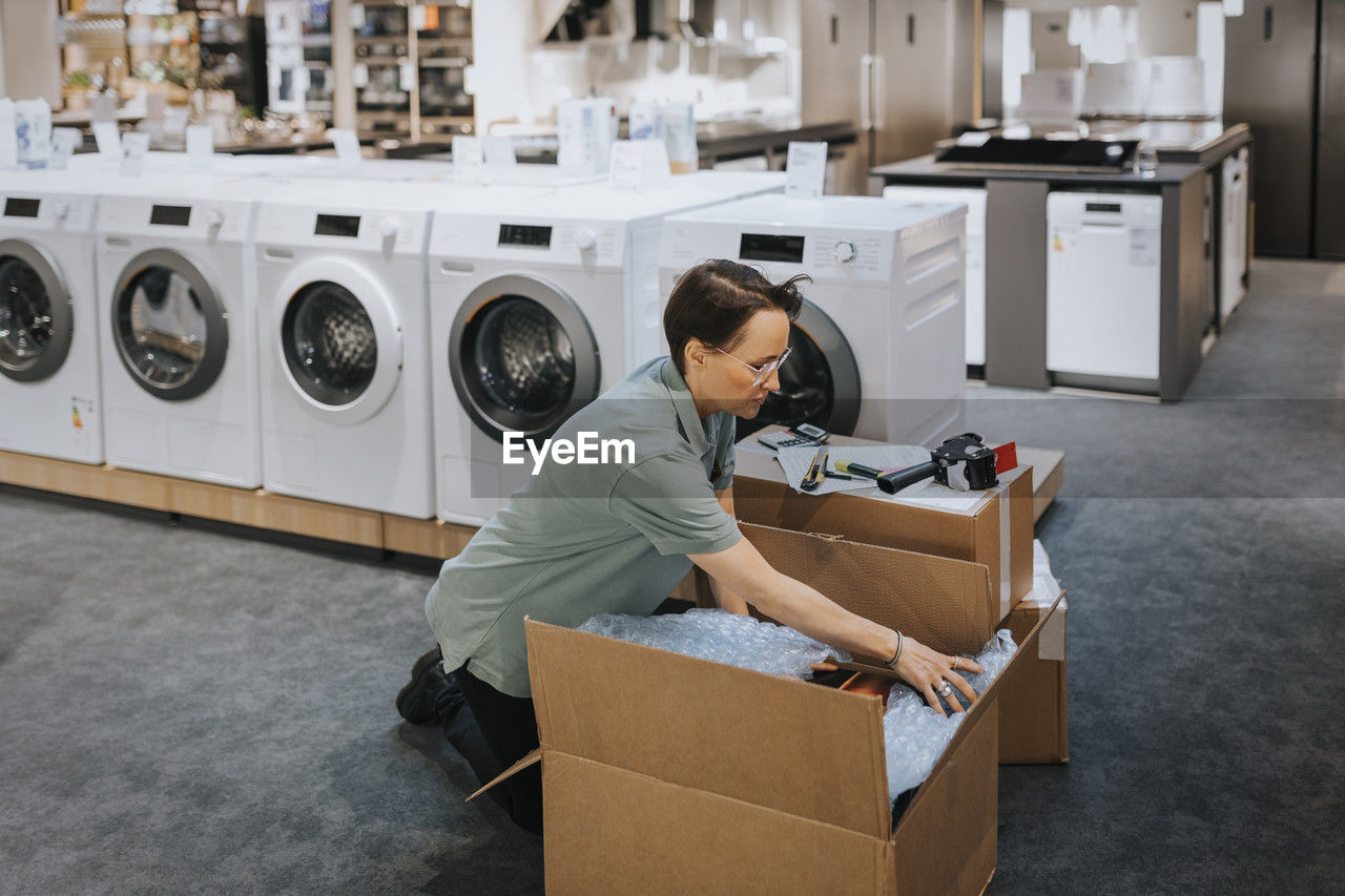 Female retail clerk opening cardboard box while working in appliances store