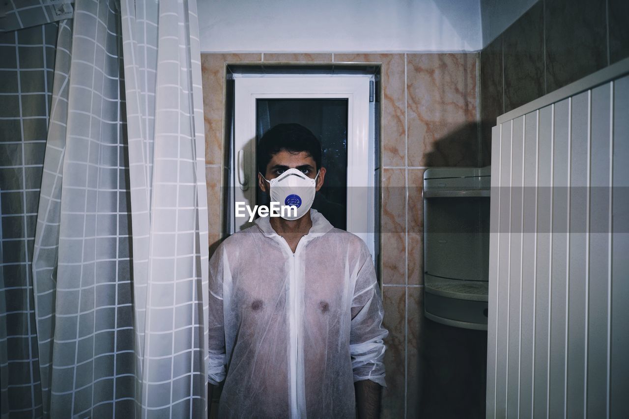 Portrait of man wearing gas mask while standing against wall at home