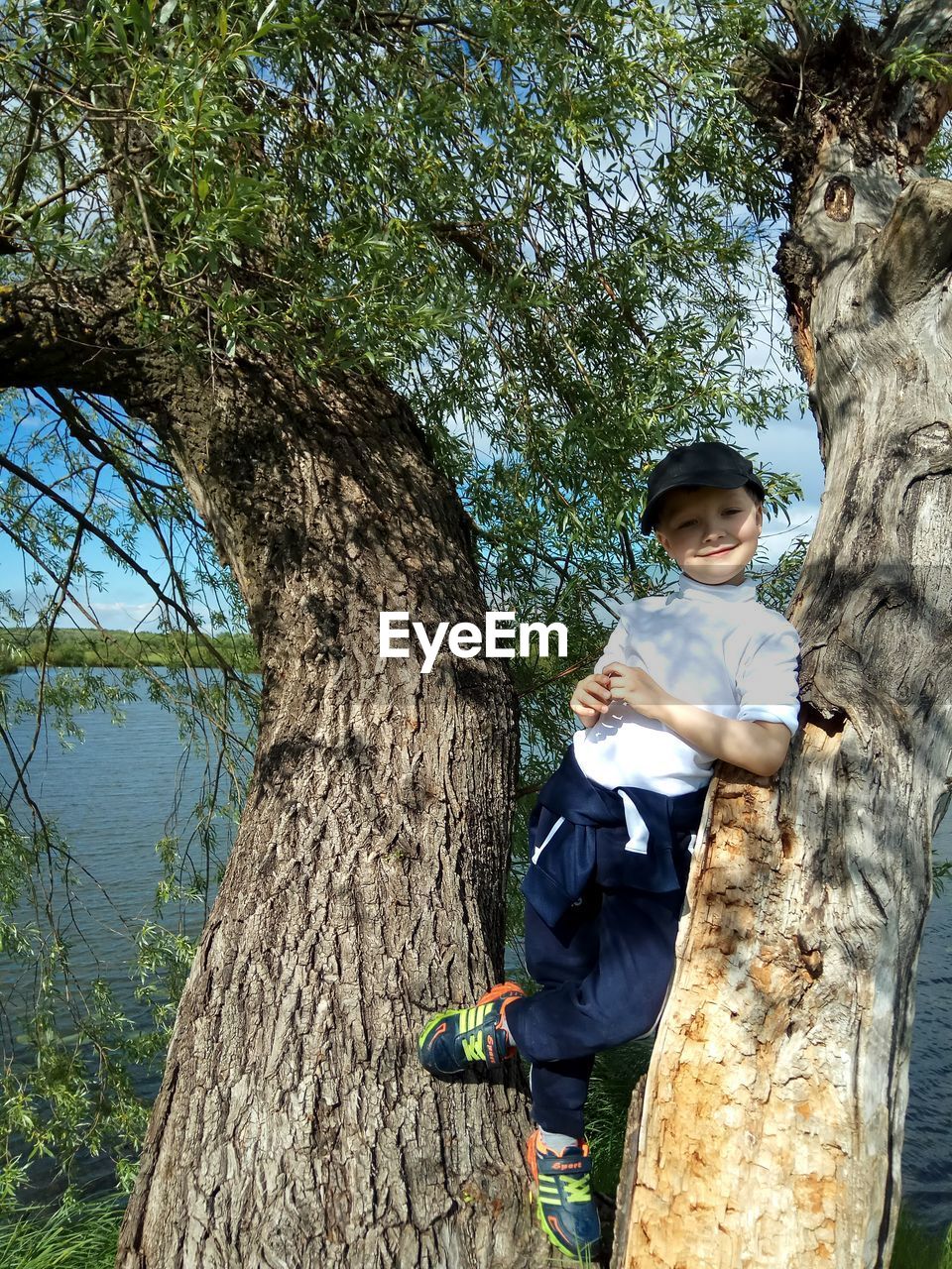 PORTRAIT OF HAPPY BOY STANDING ON TREE TRUNK