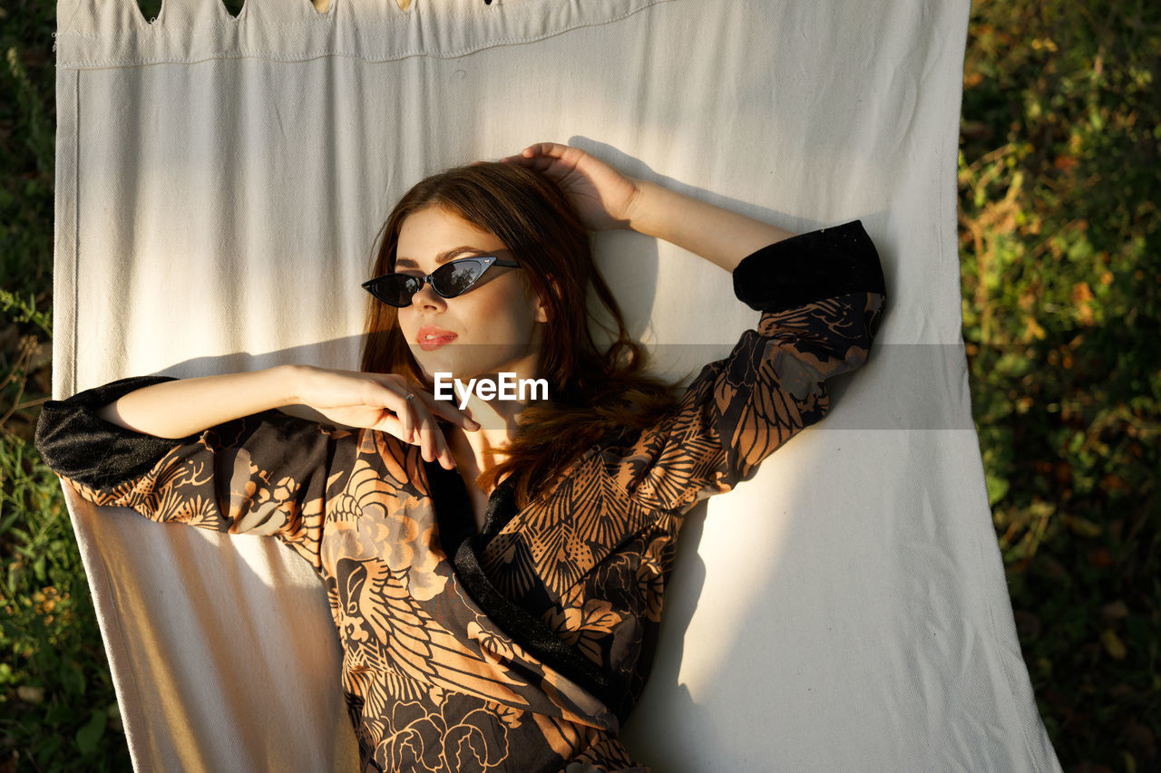 portrait of young woman wearing sunglasses against curtain