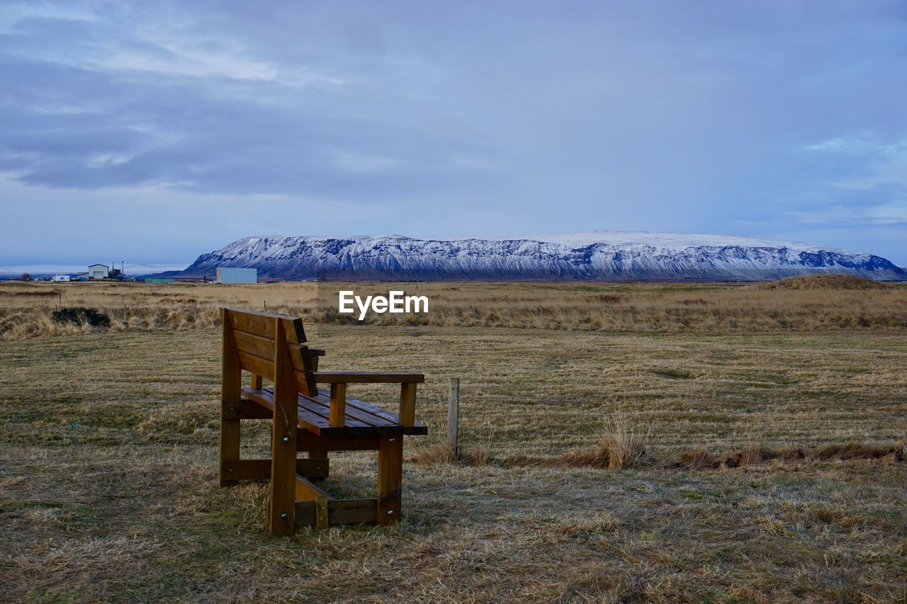 Empty bench on field against sky