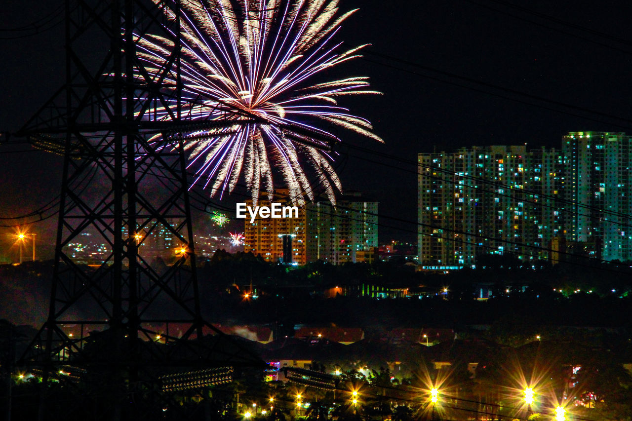 Firework display in city against sky at night