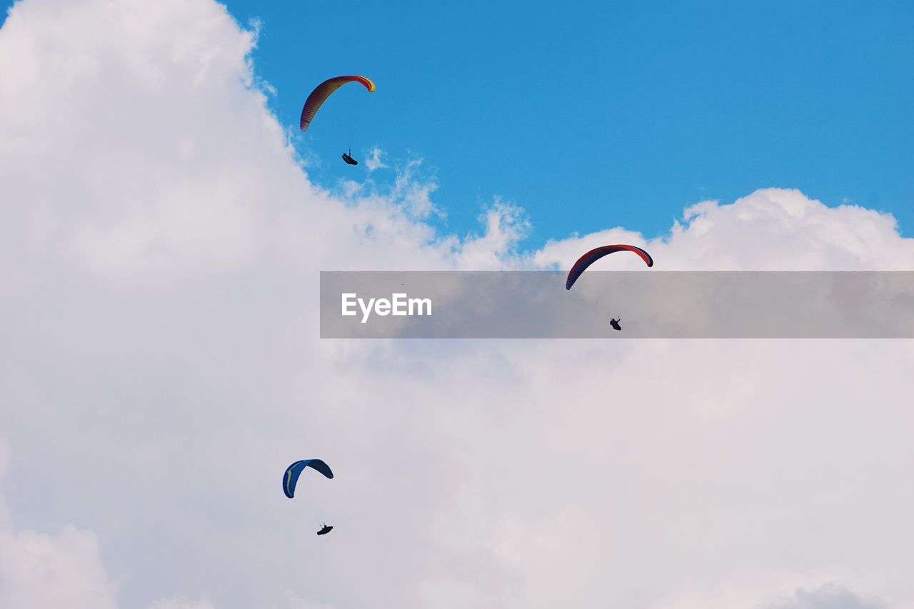 Low angle view of people paragliding against cloudy sky