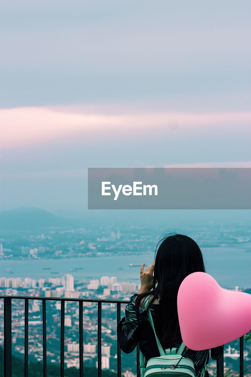 Rear view of woman with heart shape balloon at observation point against sky