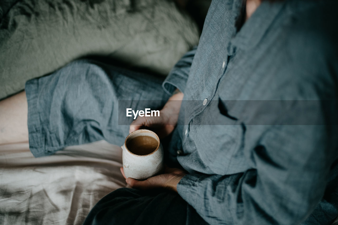 midsection of man holding coffee on bed at home