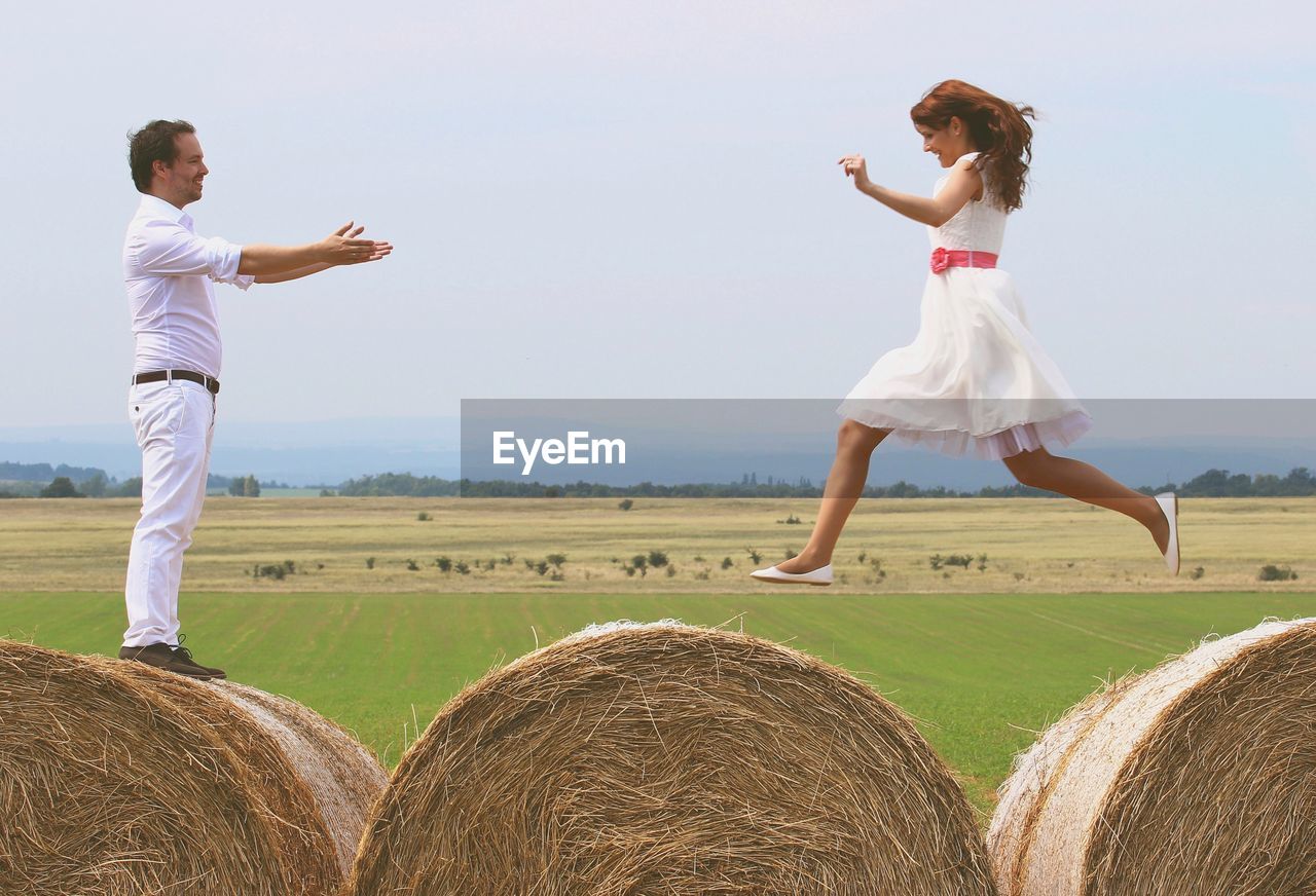 Woman jumping on hay bales towards embracing man