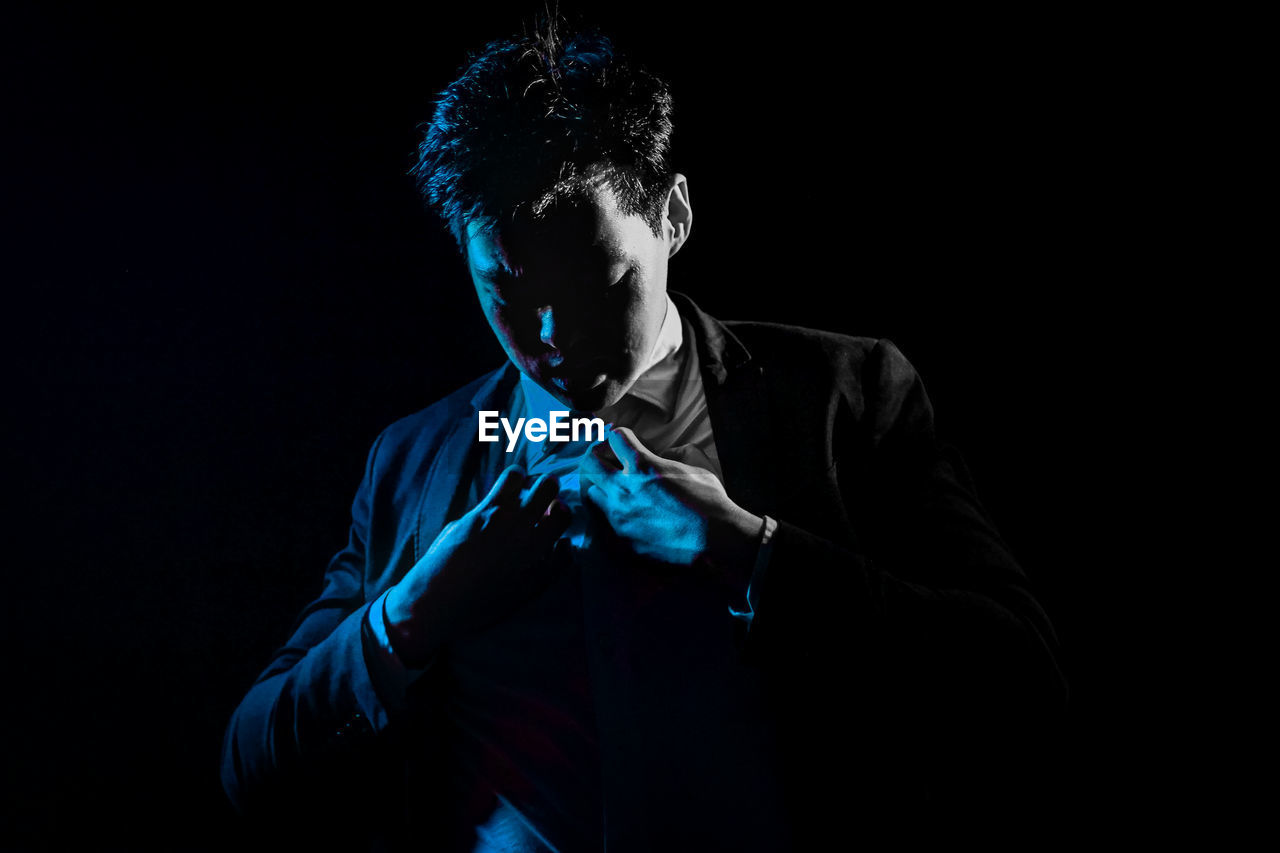 Close-up of young businessman against black background